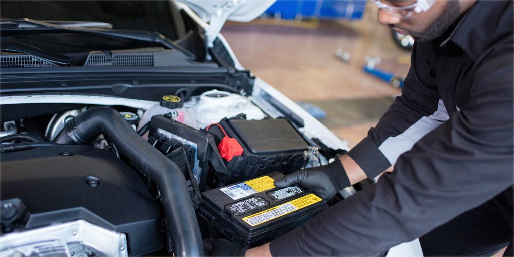 Mechanic installing a new car battery into a vehicle engine bay.