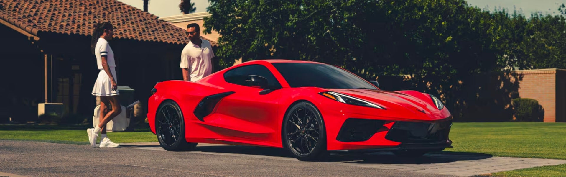Red Corvette parked with couple nearby
